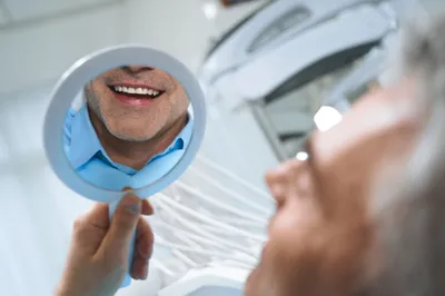 Man smiling in mirror after receiving dental implants.